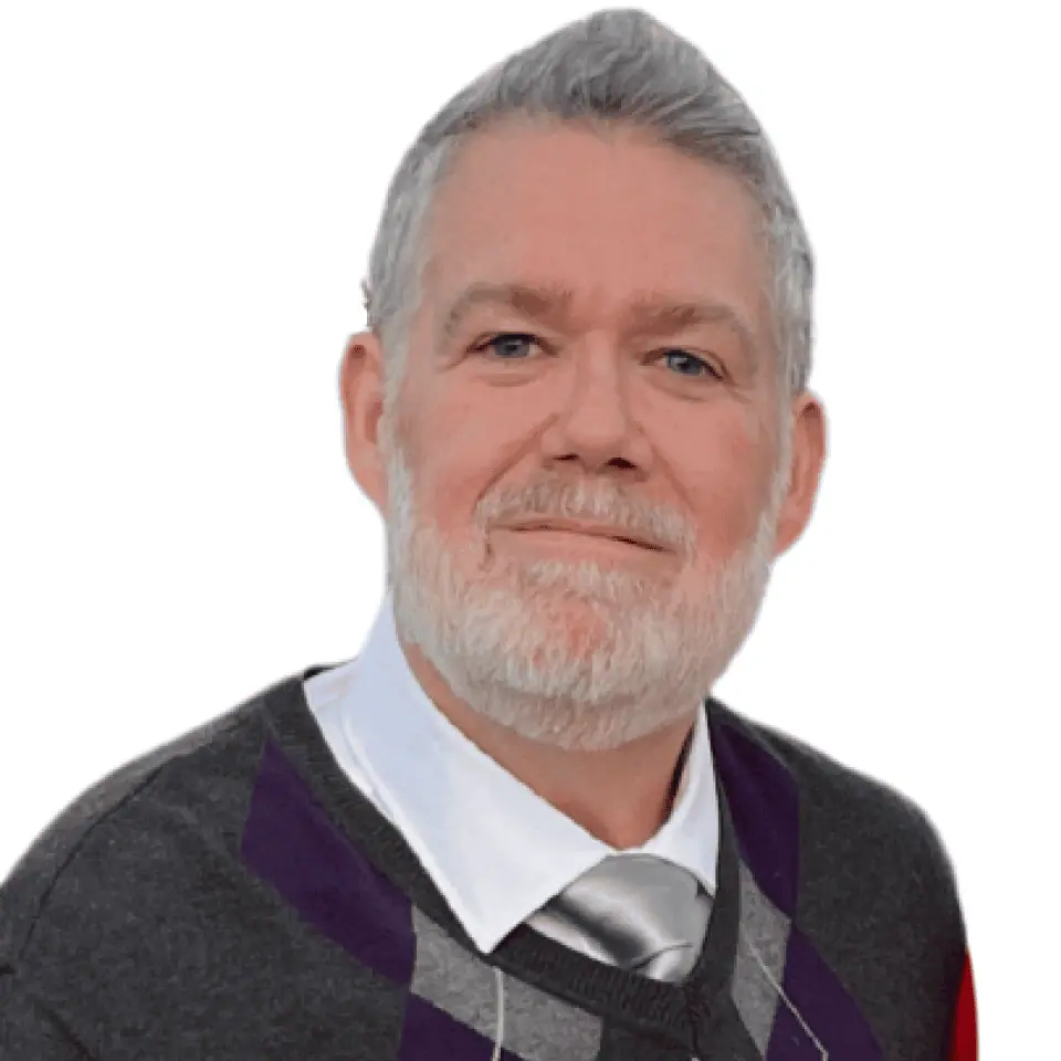 James with a gray beard and hair, wearing a gray sweater with purple accents and a white collared shirt with a silver tie, against a white background.