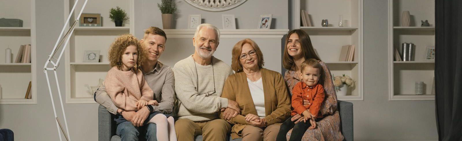 A multi-generational family sitting together on a sofa in a warm living room.