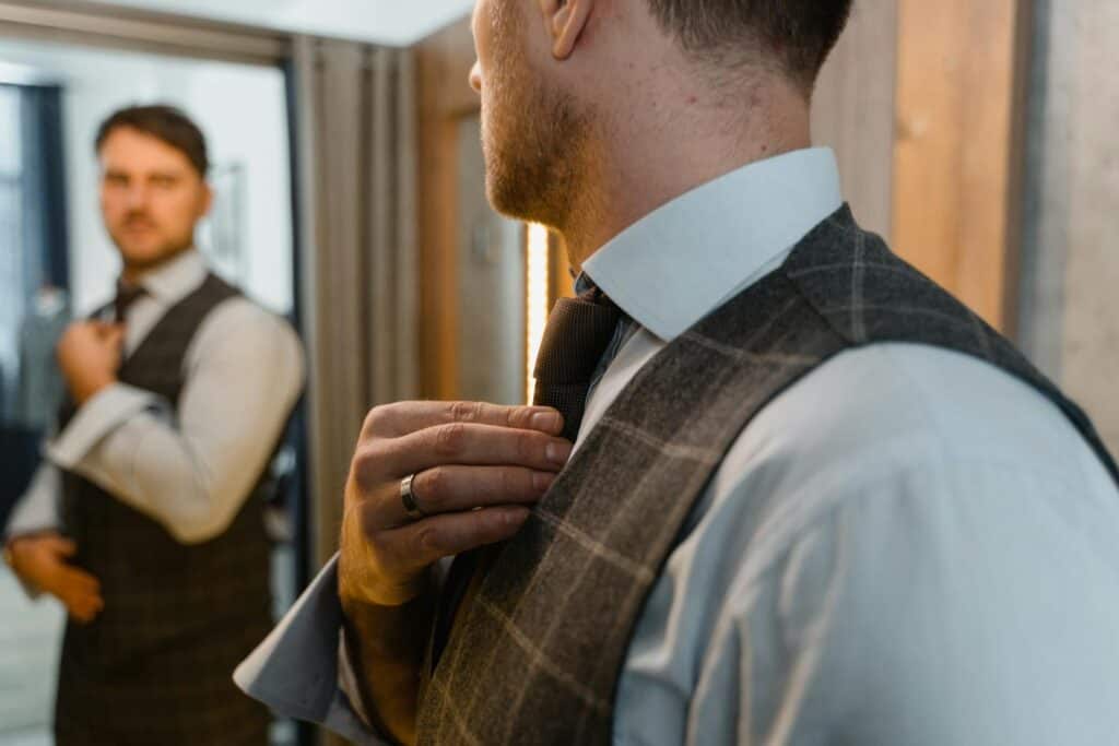 Man in a tailored suit adjusting his tie in front of a mirror, showcasing elegance and style.