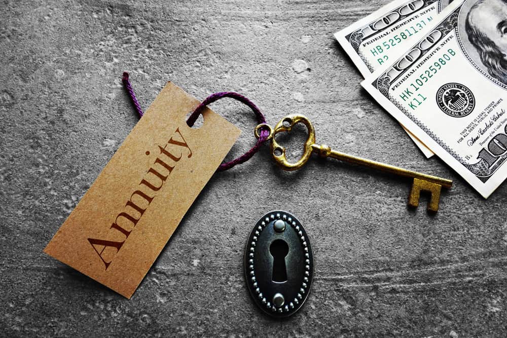A vintage key with a tag labeled "Annuity," a keyhole, and several hundred-dollar bills on a textured surface.