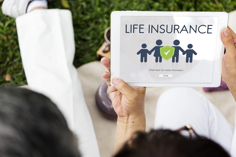 Person holding a tablet outdoors displaying a life insurance webpage with icons of people and a green check mark.