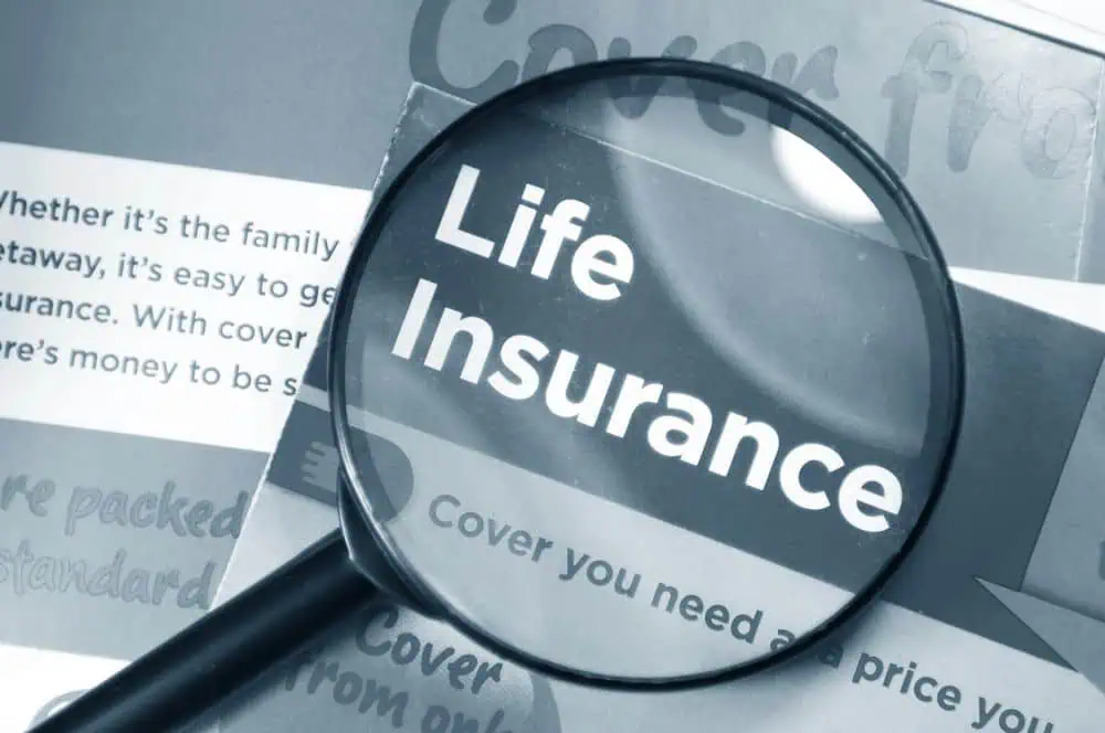 A magnifying glass highlights the words "Life Insurance" on a printed document, emphasizing the importance of the topic.