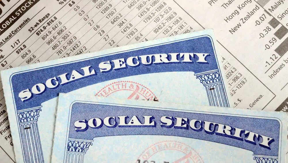 Two Social Security cards partially cover a financial newspaper showing stock market data.