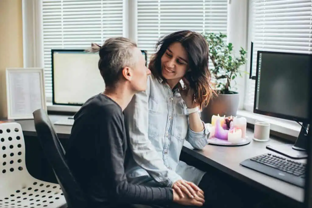 A happy couple sharing a moment together in their cozy home office with candles and technology.