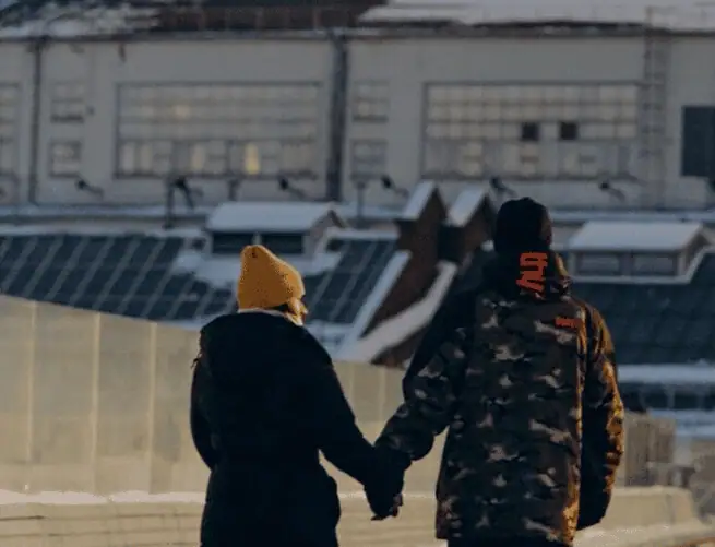 Two people holding hands walk along a snowy path, with industrial buildings and glass structures—reflecting the bustle of business tax planning Louisiana—in the background.