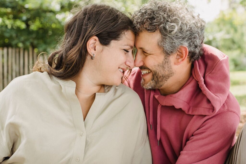 Cheerful young woman in shirt having romantic moment with happy husband with curly gray hair