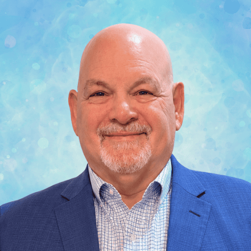 Headshot of a smiling, bald man with a goatee, wearing a blue blazer and a checkered dress shirt.