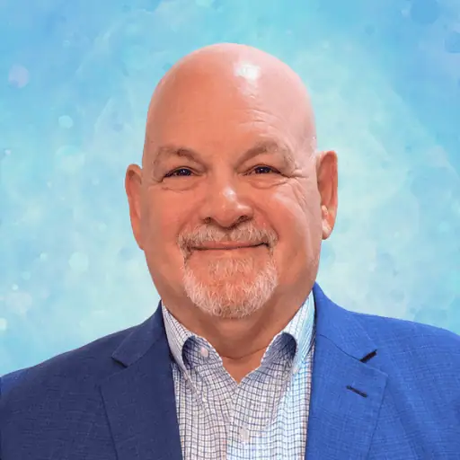 Headshot of a smiling, bald man with a goatee, wearing a blue blazer and a checkered dress shirt.